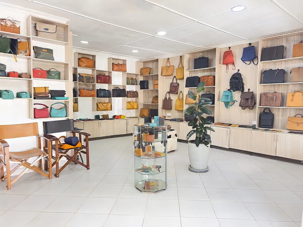 Store interior with shelves displaying various bags and a chair.