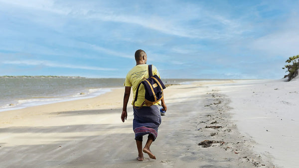 Person walking on a sandy beach with a leather backpack