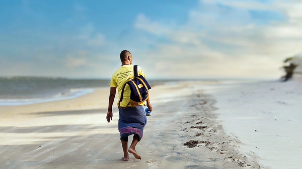 Person walking on a beach with a leather backpack