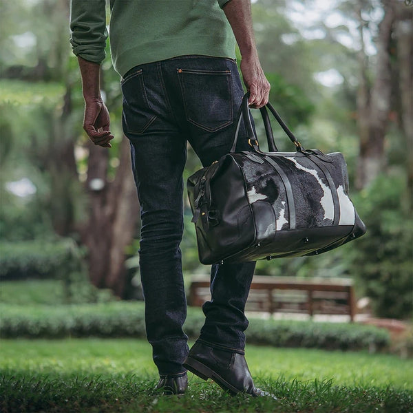 Person holding a black and white leather duffel bag in a park setting