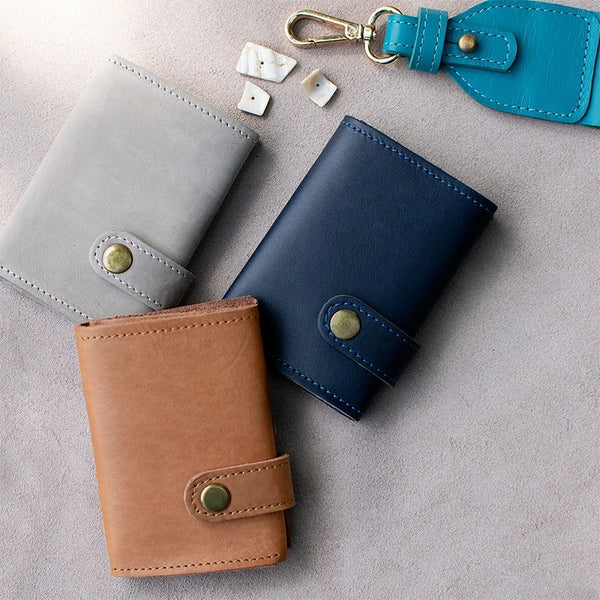 Three leather wallets in gray, blue, and brown on a light gray surface.