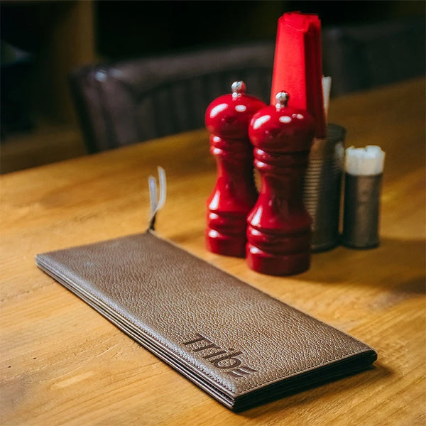 Red pepper grinder set on a wooden table with a brown leather menu.