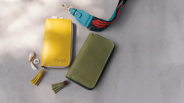 Two leather wallets, one yellow and one green, with a colorful strap on a light gray background.