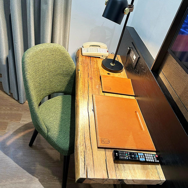 Wooden desk  with leather blotters, green chair, lamp, and electronic devices in a room.