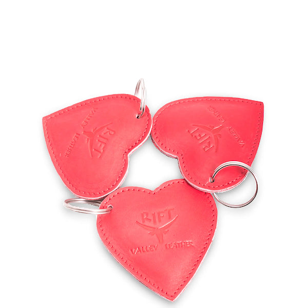 Three pink leather heart-shaped keychains with a brand logo on a white background