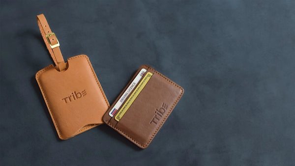 Brown leather luggage tag and cardholder with 'Tribe' branding on a dark gray background