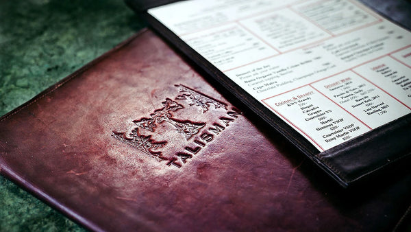 Leather-bound menu with embossed logo on a green surface
