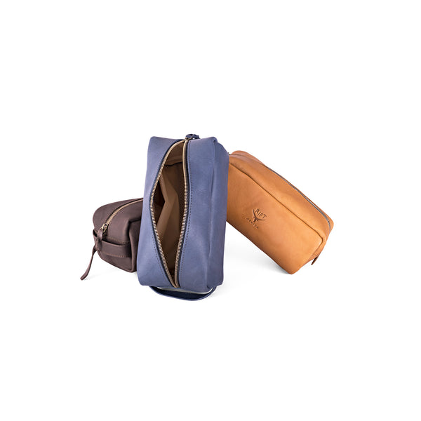 Three leather toiletry bags in blue, brown, and tan