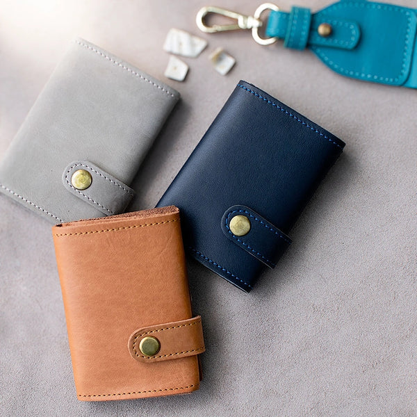 Three leather wallets in gray, blue, and brown on a gray surface.