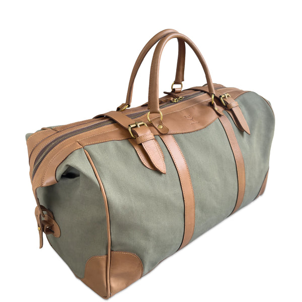 A canvas duffel bag in muted sage green with tan leather handles, straps, and corner protectors, shown on a plain white background.
