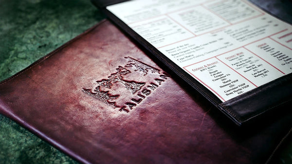 Brown leather menu cover with embossed logo on a green surface
