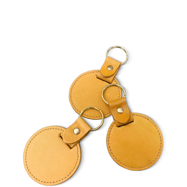 Three tan leather keychains with gold rings on a white background